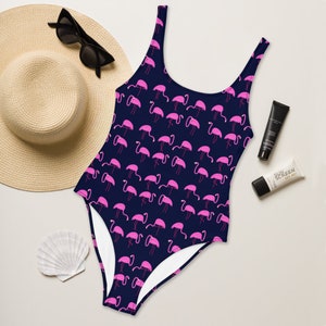 May include: A navy blue one-piece swimsuit with a pink flamingo print. The swimsuit has a scoop neck and thin straps.