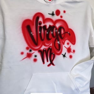May include: White hoodie with a red and black airbrushed design that says "Virgo Me" with rhinestones. The hoodie has a pocket and the text "#AIRBRUSHHOODIE" is printed on the bottom.