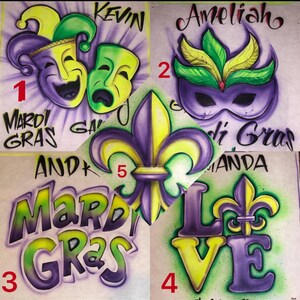 May include: Airbrushed designs with a Mardi Gras theme. Features a jester mask, a masquerade mask, the words "Mardi Gras", a fleur-de-lis, and the word "LOVE" with a fleur-de-lis. The designs are in purple, yellow, and green.