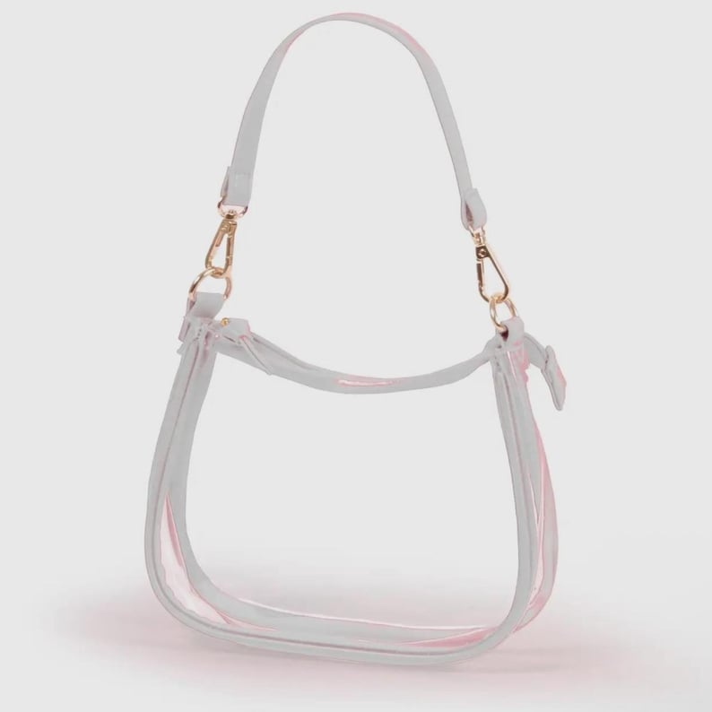 May include: A clear, transparent handbag with a white trim and a pink accent. The bag has a shoulder strap and gold-colored clasps. The bag is designed with a curved shape.