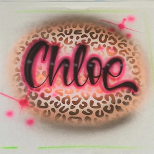 May include: A circular airbrushed design with the name "Chloe" in black script and a pink outline. The background features a leopard print pattern in brown and tan, with pink accents.