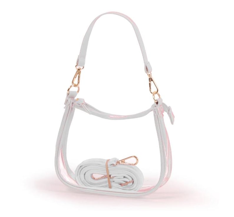 May include: A clear, white, and pink handbag with a shoulder strap and a detachable crossbody strap. The bag has gold-colored hardware and a curved design. The crossbody strap is rolled up and secured with a rubber band.