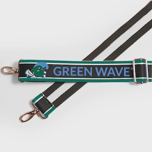 May include: A black and green shoulder strap with the text "GREEN WAVE" in blue. The strap features a Tulane University logo and gold-colored metal hardware. The strap has a white stripe and a black stripe.