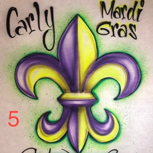 May include: A purple and yellow fleur-de-lis design with the words "Carly Mardi Gras" in black script. The number "5" is in red. The background is light green with a speckled effect.