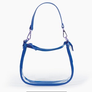 May include: A clear handbag with a bright blue trim, handle, and shoulder strap. The bag has silver-coloured metal clasps and a zip closure. The design is simple and modern, suitable for various occasions.
