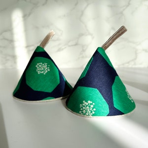 May include: Two green and navy blue pot holders with a white floral pattern. The pot holders are shaped like cones and have a loop handle.