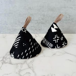 May include: Two black and white patterned pot holders with a tan loop handle. The pot holders are shaped like cones.