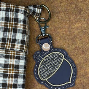 May include: A white ceramic mug with a black handle and the text "But First, Coffee" in a bold, black font. The mug is set against a blurred background, suggesting a cozy setting. The mug appears to be approximately 4 inches tall.