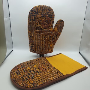 May include: A set of two brown and yellow oven mitts with a geometric pattern. The mitts are made of fabric and have a brown trim.
