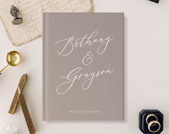 May include: A light brown wedding planner with the names "Bethany & Grayson" written in white cursive script. The text "Wedding Planner" is printed in white at the bottom of the cover.