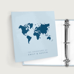 May include: A light blue binder with a dark blue world map design. The text "THE ADVENTURES OF EMILY & AUSTIN" is printed below the map. The binder is open, revealing white pages and a silver metal ring binder mechanism.