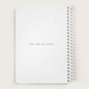May include: White spiral bound notebook with the text "YOU ARE SO LOVED" printed in gold on the front cover.