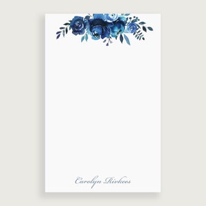 Op de afbeelding: Notitieboekje met een blauw aquarel bloemenontwerp met de naam "Carolyn Rivkees" onderaan gedrukt.
