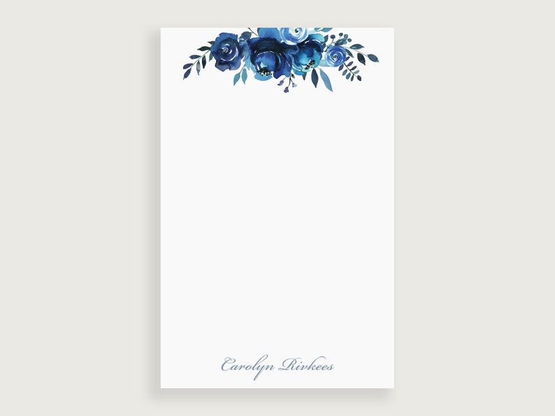 Op de afbeelding: Notitieboekje met een blauw aquarel bloemenontwerp met de naam "Carolyn Rivkees" onderaan gedrukt.
