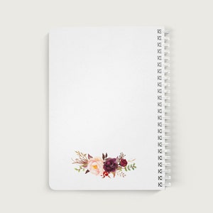 May include: A white spiral bound notebook with a floral design on the bottom right corner. The flowers are pink, red, and burgundy.