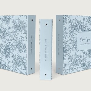 May include: Three light blue binders with a floral pattern. The binders are labeled "Emily's Family Recipes" and feature a square label with the name "Emily's" on the front. The floral design is in a darker blue.
