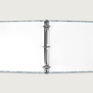 May include: Open binder with a light blue floral patterned cover. The binder is open, revealing blank white pages. The metal rings are visible in the center. The cover has a light blue background with a white floral design.