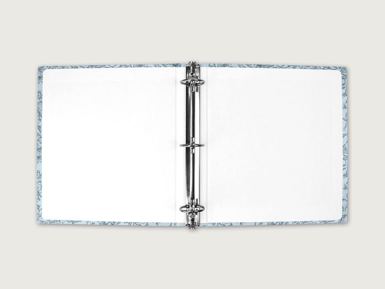 May include: Open binder with a light blue floral patterned cover. The binder is open, revealing blank white pages. The metal rings are visible in the center. The cover has a light blue background with a white floral design.