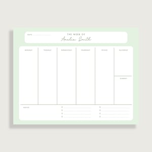 May include: A weekly planner notepad with a soft green border. The top section includes the text "THE WEEK OF Amelia Smith". The days of the week are listed, with space for notes and bullet points at the bottom. The notepad is designed for organization.