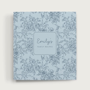 May include: A light blue recipe binder with a floral pattern. The cover features a square label with the text "Emily's Family Recipes" in a script font. The floral design includes detailed drawings of flowers and leaves.