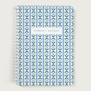 May include: Spiral-bound notebook with a floral pattern. The cover features a repeating design of blue and green flowers and vertical stripes on a white background. The name "KIMBERLY MADDAN" is printed on a white rectangle.