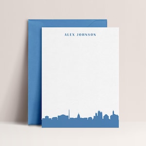May include: White stationery with a blue envelope. The stationery features the name "ALEX JOHNSON" at the top and a blue skyline design at the bottom. The stationery is a simple and elegant design.