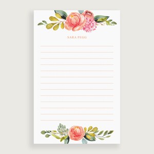 May include: A white notepad with a watercolor floral design. The top and bottom of the notepad feature pink and peach flowers with green leaves. The text "SARA PEGG" is printed in a copper color above the lined paper.
