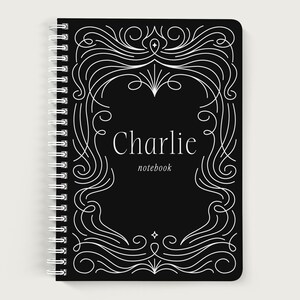 May include: Black spiral-bound notebook with a white decorative frame design. The notebook cover features the name "Charlie" and the word "notebook" in white lettering. The design is a stylized, elegant frame.