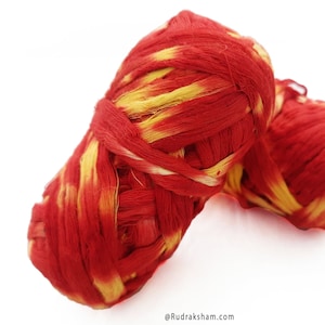 Puede incluir: Dos ovillos de hilo rojo y amarillo, atados juntos. El hilo es una mezcla de rojo y amarillo, creando un efecto a rayas.