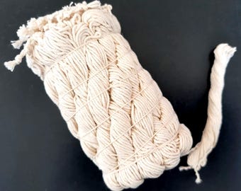May include: A close-up of a large roll of natural cotton twine. The twine is tightly wound and has a natural, off-white color.