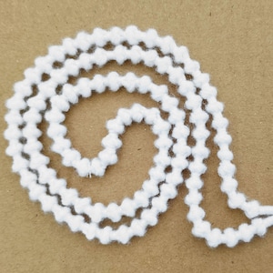Könnte beinhalten: Weißer, flauschiger Besatz mit einer perligen Textur. Der Besatz ist spiralförmig aufgerollt.