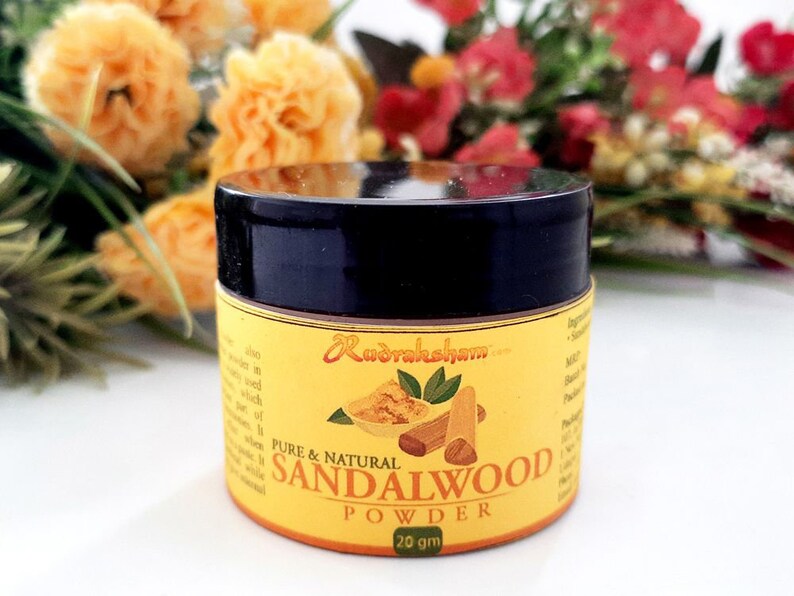 May include: A small, round jar of sandalwood powder with a black lid. The jar is labeled "Pure & Natural Sandalwood Powder 20 gm" and features a small image of sandalwood sticks and leaves.