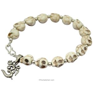 May include: White skull bead bracelet with a silver Om charm. The bracelet is made of white beads with a skull design and silver spacers. The Om charm is attached to the bracelet with a silver loop.