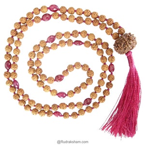 May include: A brown and red mala bead necklace with a tassel. The beads are made of rudraksha seeds and the tassel is made of red thread. The necklace is 108 beads long and is used for meditation and prayer.