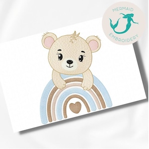 May include: Embroidered design of a brown bear sitting on a rainbow with a heart in the center. The rainbow is made of blue, pink, and brown stripes.