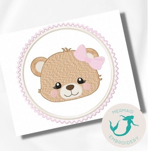 Può includere: Disegno ricamato di un orso marrone con fiocco rosa, all'interno di un cerchio bianco con bordo rosa a festoni. Il disegno è su uno sfondo bianco con un cerchio rosa e bianco con il testo "Mermaid Embroidery" e una silhouette di sirena turchese.