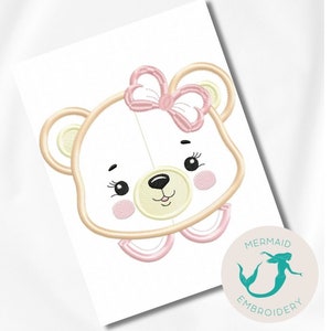 Pode incluir: Desenho bordado de um urso branco com bochechas cor-de-rosa, um laço rosa e um contorno castanho claro. O urso está olhando para a direita. O desenho está sobre um fundo branco.