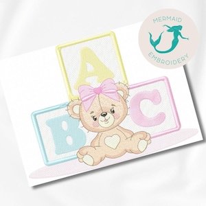 Pode incluir: Um desenho bordado com um urso de pelúcia com um laço rosa, em frente a três blocos do alfabeto. Os blocos são em cores pastel com as letras A, B e C. O desenho inclui o texto "Mermaid Embroidery".