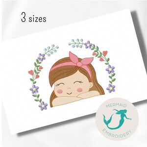 Pode incluir: Desenho bordado de uma menina com cabelo castanho usando uma faixa de cabeça rosa, sorrindo e olhando para baixo. A menina está cercada por uma coroa de flores rosa, roxas e azuis.