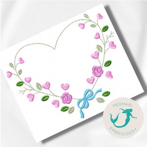 Pode incluir: Desenho bordado de uma coroa de coração com rosas cor-de-rosa e corações, fita azul e folhas verdes. O desenho está sobre um fundo branco. O texto "MERMAID EMBROIDERY" está em um círculo abaixo do desenho.