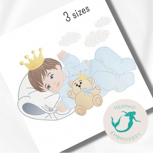 Peut inclure: Broderie représentant un bébé garçon portant une couronne et un pyjama, dormant sur un oreiller avec un ours en peluche. Le motif comprend des nuages et le texte "3 tailles".