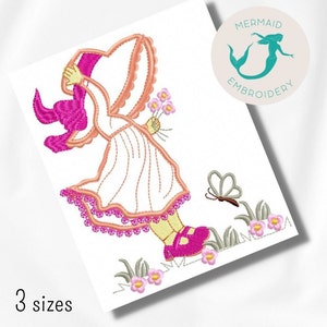 May include: An embroidered design featuring a girl in a bonnet and dress, holding flowers, with a butterfly and floral accents. The design is in shades of pink, peach, and white, with the text "3 sizes" at the bottom and a logo in the upper right corner.