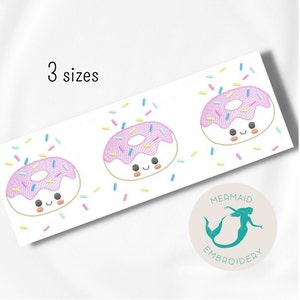 Pode incluir: Três donuts rosa e branco com granulado e um rosto sorridente. Os donuts estão dispostos em uma fila sobre um fundo branco com granulado espalhado ao redor deles. O texto "3 tamanhos" está na parte superior da imagem. O texto "Mermaid Embroidery" está na parte inferior da imagem em um círculo com uma sereia dentro.