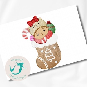 May include: Embroidered design of a gingerbread stocking with a girl wearing a red and white hat and scarf inside. The stocking has a white tree and hearts on it.