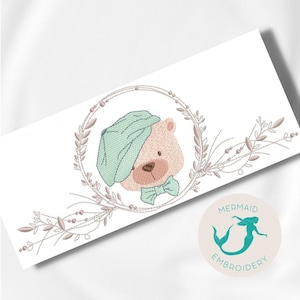 Pode incluir: Desenho bordado de um urso fofo usando um chapéu verde e uma gravata borboleta, rodeado por uma coroa de folhas e bagas. O design é perfeito para um berçário ou um quarto de criança.