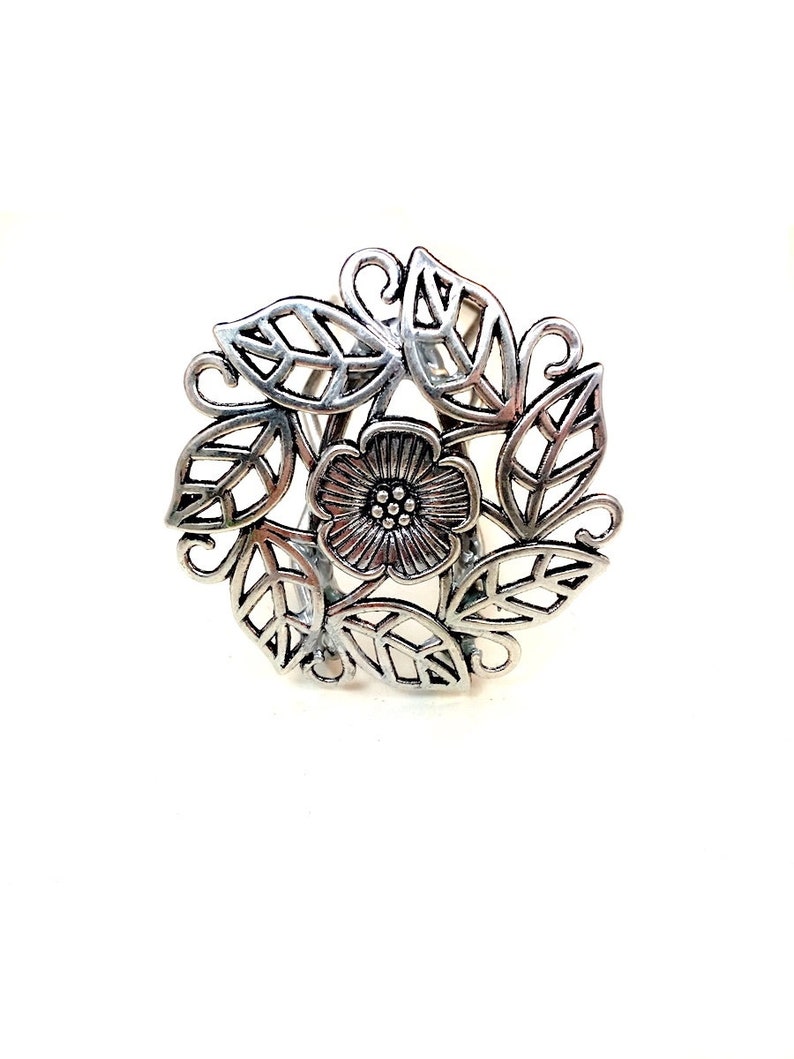 Pu&ograve; includere: Anello floreale in argento con un design delicato che presenta un fiore con un centro di piccoli punti circondati da foglie.