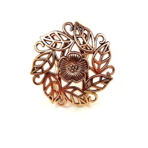 Pu&ograve; includere: Un fermaglio per capelli in metallo dorato con un design floreale. Il fermaglio presenta un fiore centrale con dettagli intricati e foglie che lo circondano.