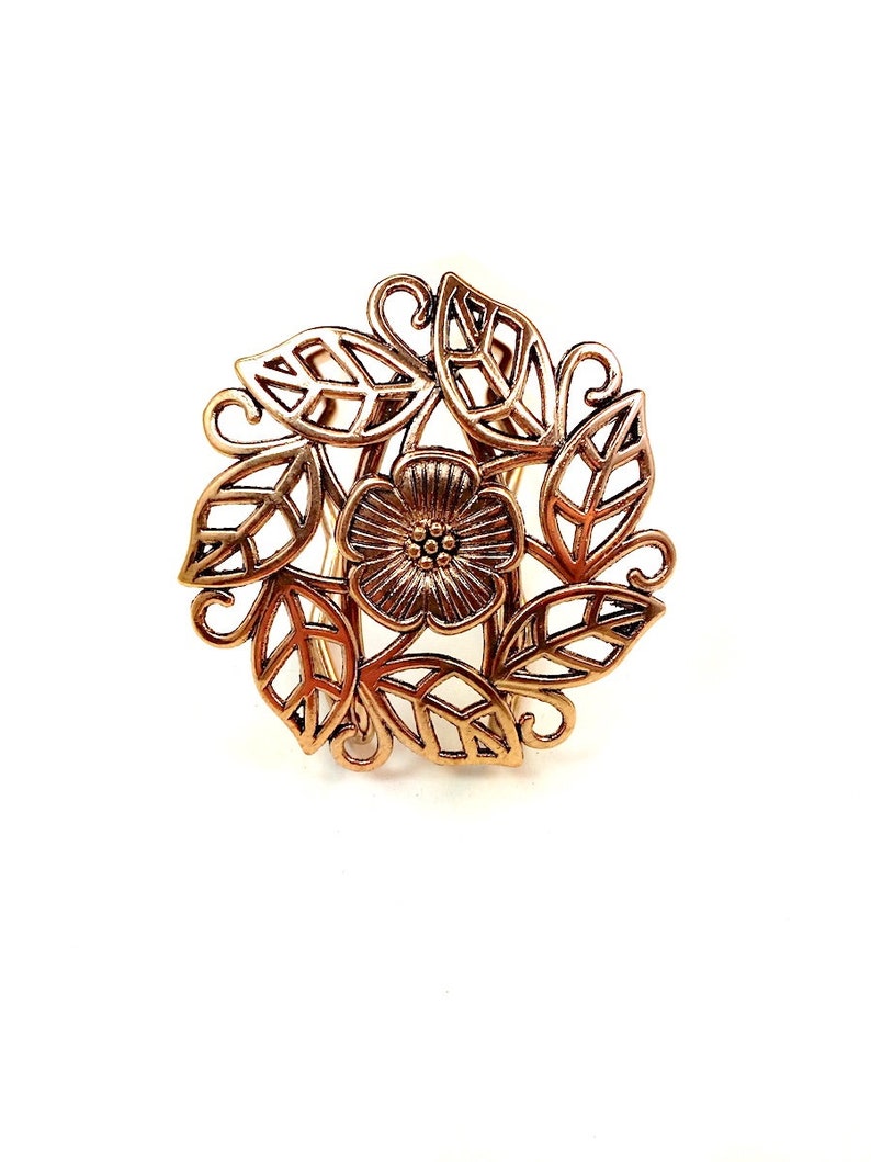 Pu&ograve; includere: Un fermaglio per capelli in metallo dorato con un design floreale. Il fermaglio presenta un fiore centrale con dettagli intricati e foglie che lo circondano.