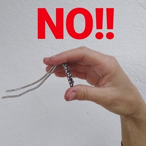 Pu&ograve; includere: Una mano che tiene una forcina per capelli argentata con strass neri. La parola "NO!" &egrave; scritta in lettere rosse sopra la mano.