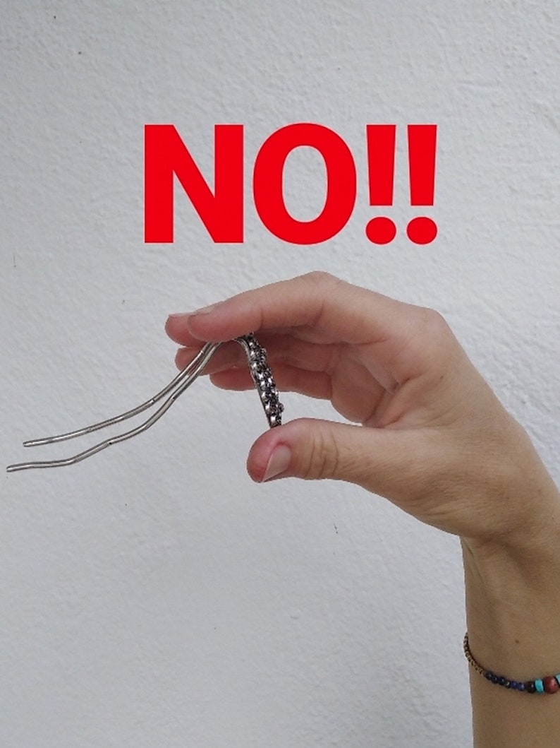 Pu&ograve; includere: Una mano che tiene una forcina per capelli argentata con strass neri. La parola "NO!" &egrave; scritta in lettere rosse sopra la mano.